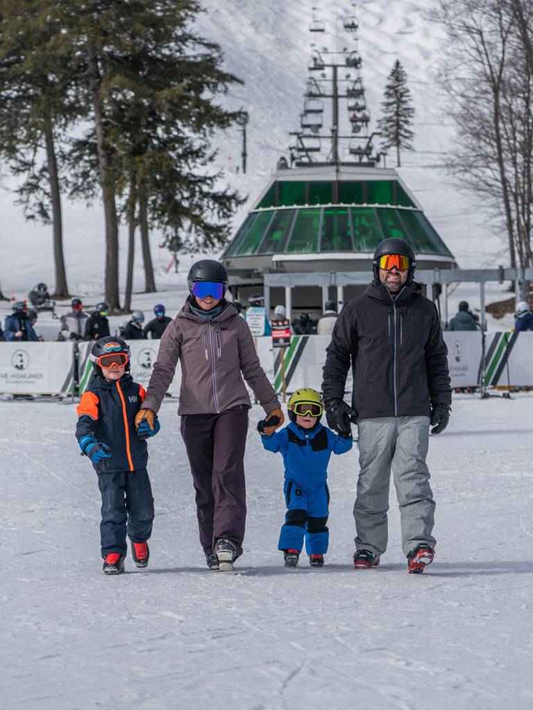 A family in ski gear walking in front of a ski lift