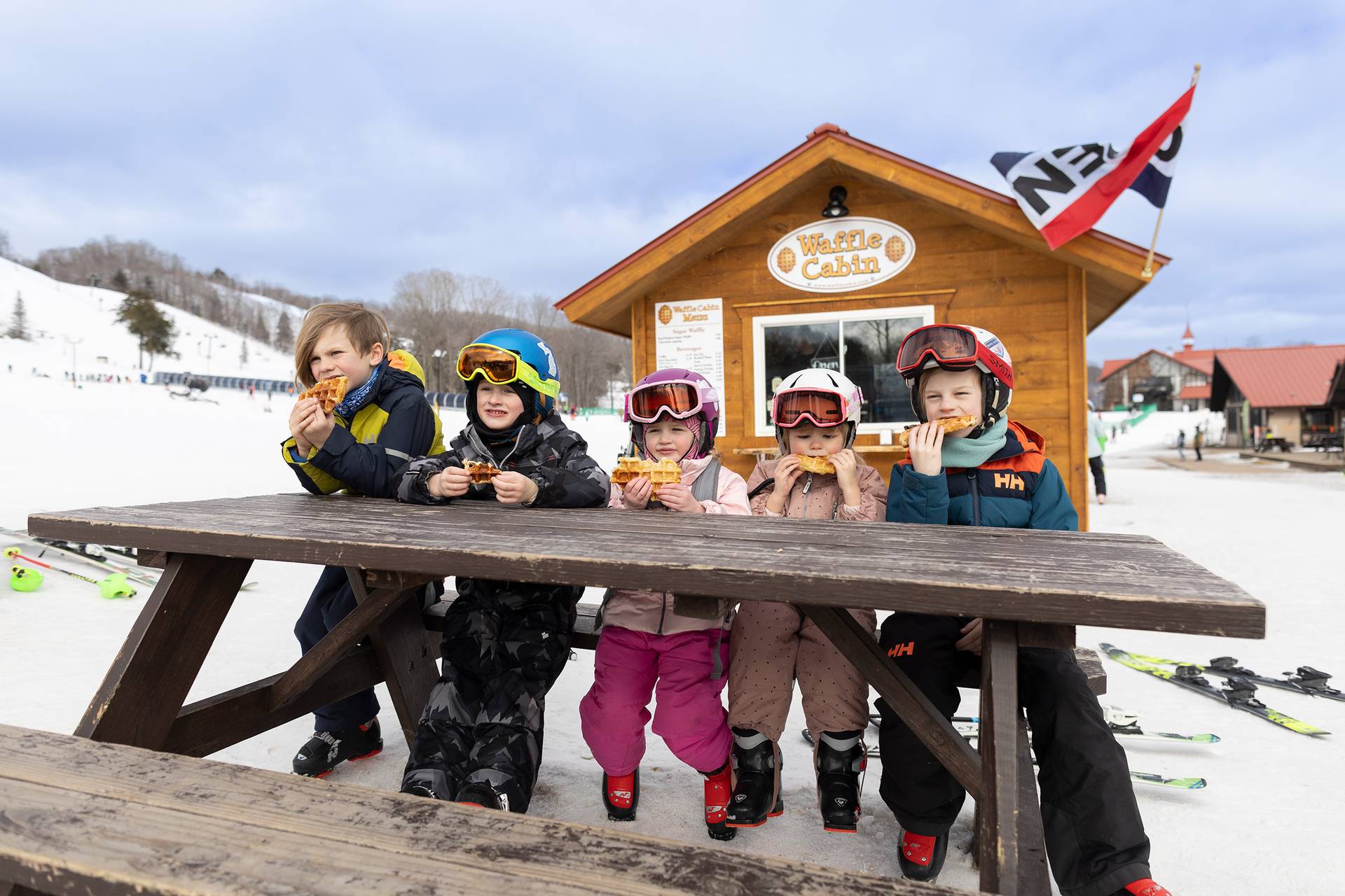 A group of kids eating a waffle in front of the waffle cabin