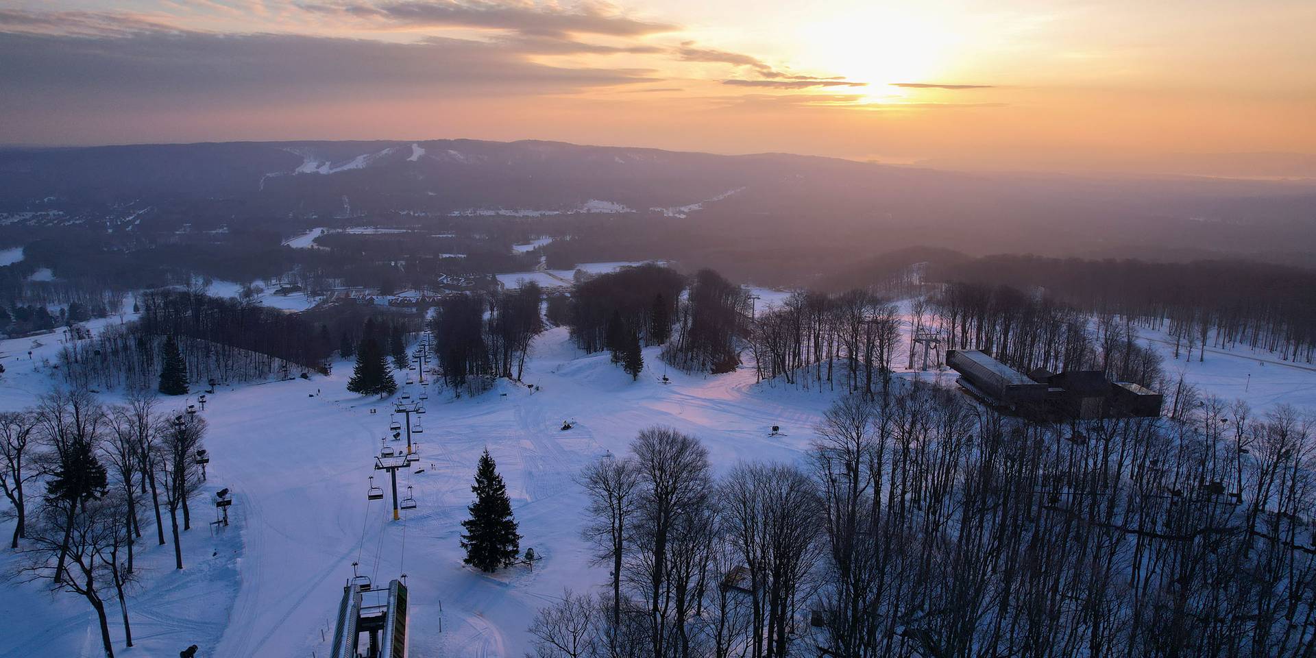 A drone shot of a sunrise over Heather and Camelot chairlifts in winter at The Highlands
